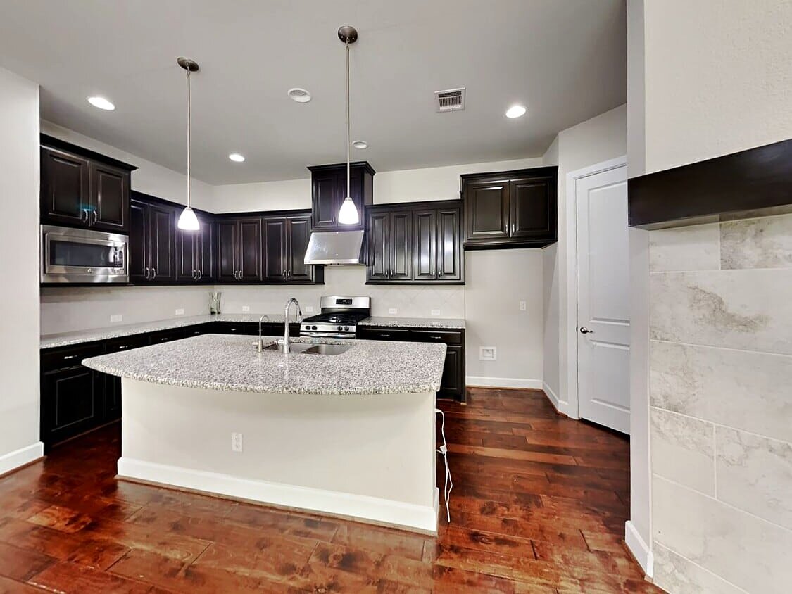Granite island kitchen with dark cabinetry and stainless steel appliances
